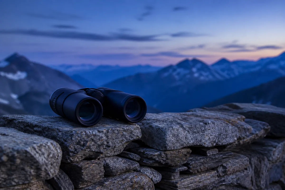Jumelles posées sur un muret face à un horizon de montagnes au crépuscule