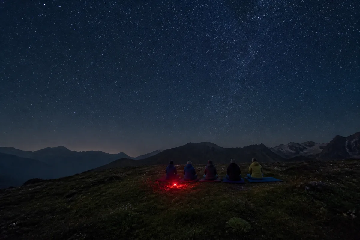 Groupe familial installé sur des tapis de sol face à un ciel nocturne dégagé en montagne